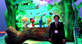 Satoru Iwata standing in front of the Pikmin 3 E3 booth.